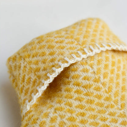 A close up of a  bright yellow wool hot water bottle with a beehive pattern, on a white background.